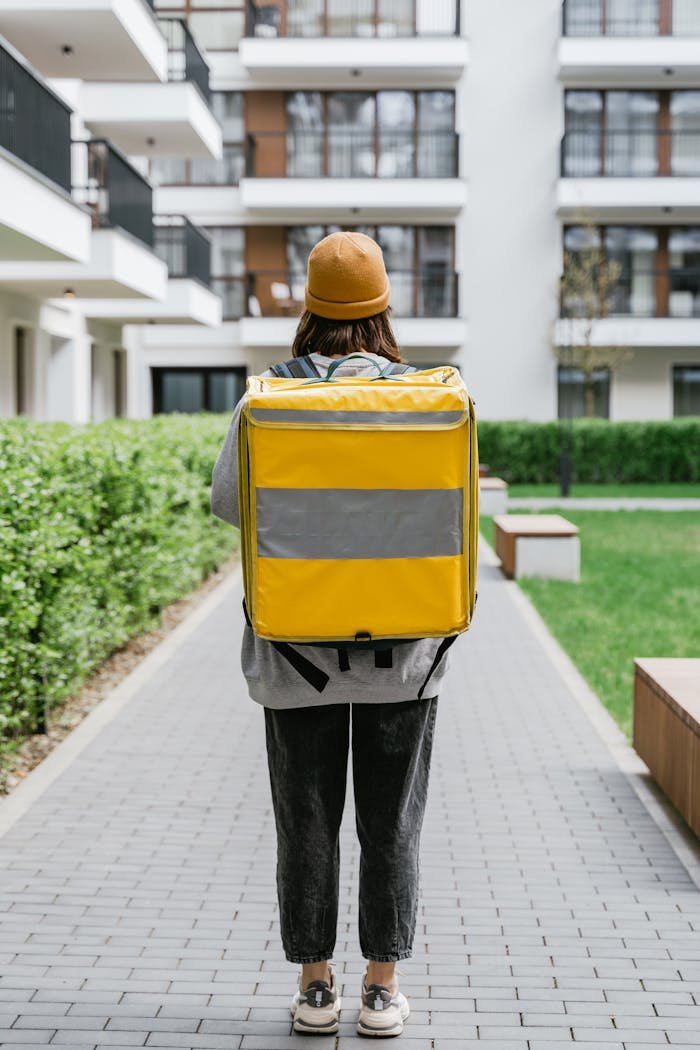 Rear view of a delivery person with a yellow thermal bag in an urban setting. Perfect for logistics themes.